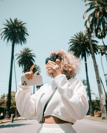 Woman in sunglasses holding a phone on a palm-lined street