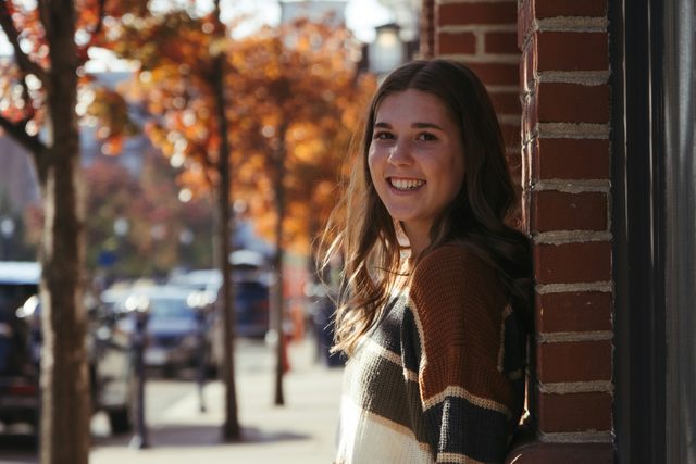 Smiling woman leaning on a brick wall on an autumn street