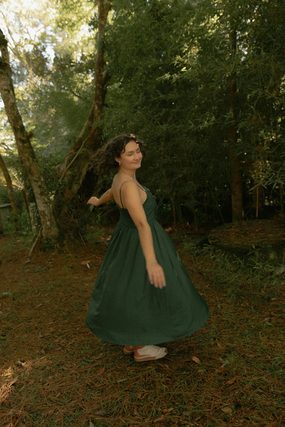 Woman in a green dress twirling among trees in a forest