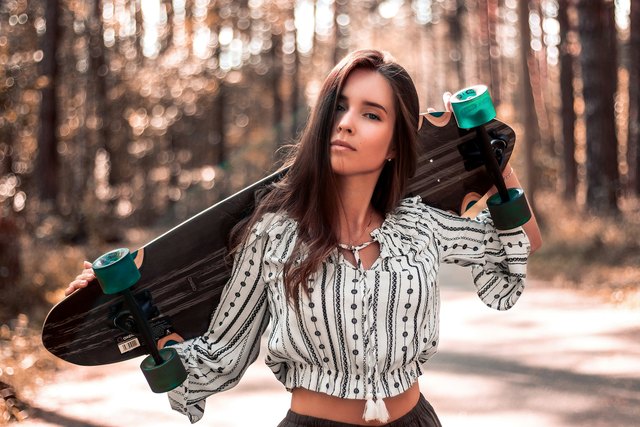 Woman holding a skateboard on a forest road