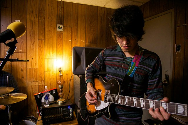 Young man playing an electric guitar in a wood-paneled room