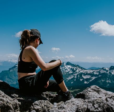 Woman in a cap sitting on rocks above snowy mountains