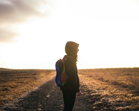 Hiker with a backpack on a field path at sunset
