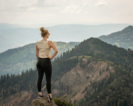 Woman standing on a ridge overlooking forested mountains