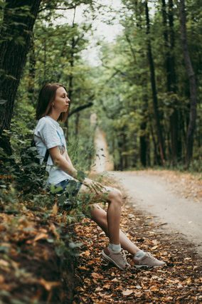 Woman sitting on a leafy bank beside a forest road