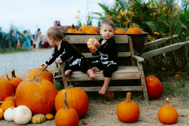 Two toddlers in skeleton costumes sitting on a cart with pumpkins