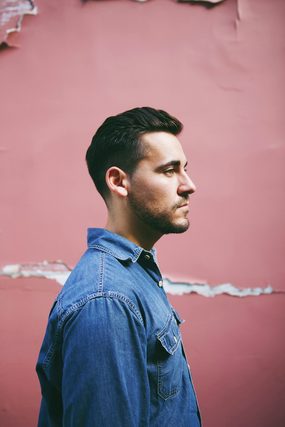 Man in a denim shirt in profile against a pink wall