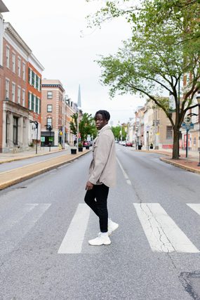 Young man in a beige jacket crossing a town street