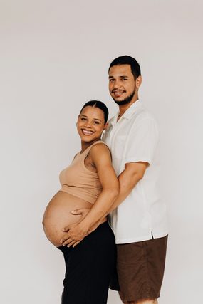 Pregnant woman and smiling man posing against a white wall