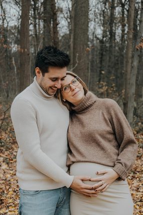 Expecting couple in sweaters embracing in an autumn forest
