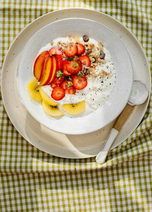 Yogurt bowl with strawberries, peach and kiwi on a checked cloth