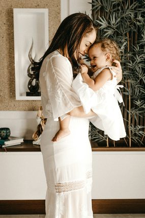 Mother in a white dress hugging her smiling toddler at home