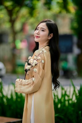 Woman in a tan tunic holding a sprig of white flowers