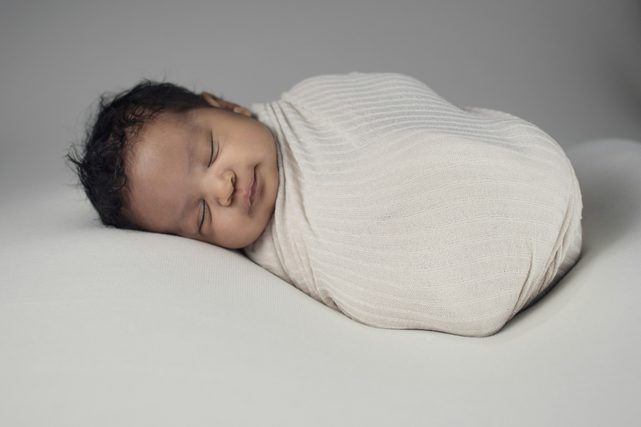 Sleeping newborn swaddled in a cream wrap on grey