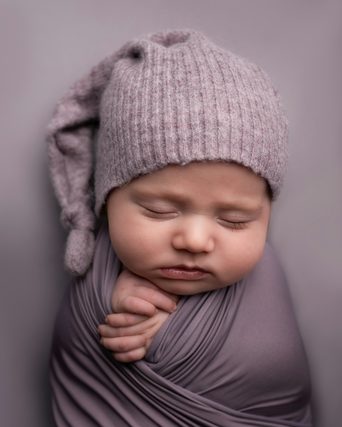 Sleeping newborn in a knit hat wrapped in mauve fabric