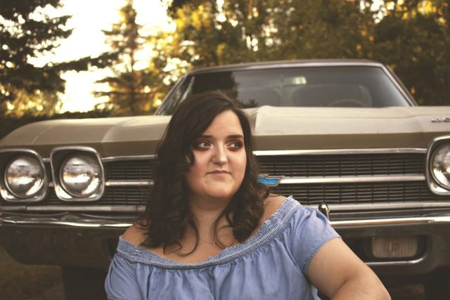 Woman in an off-shoulder blue top in front of a classic car