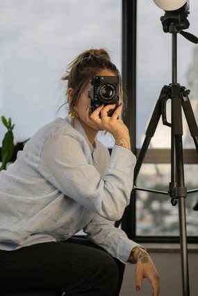 Woman in a light blue shirt aiming a camera near a tripod