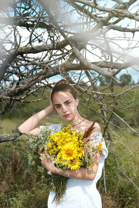 Woman in a white dress holding sunflowers under bare branches