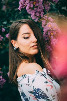 Woman in an off-shoulder floral top beside purple blossoms