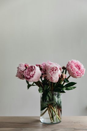 Pink peonies in a clear glass vase on a wooden table