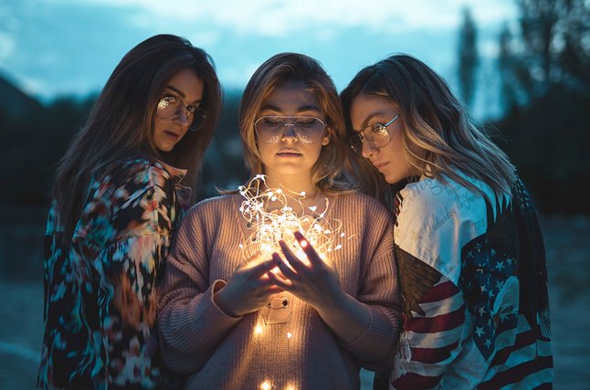 Three friends holding fairy lights at dusk