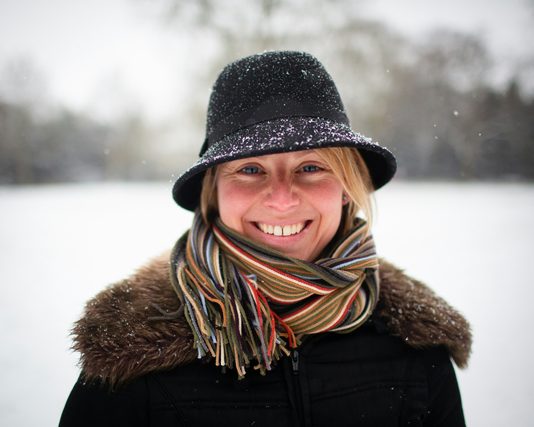 Smiling woman in a snow-dusted hat and striped scarf