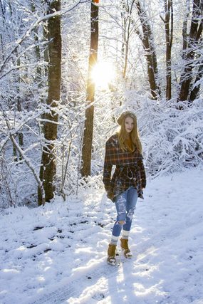 Woman in a plaid shirt walking a snowy forest path in sunlight