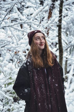 Woman in a knit hat and scarf among snow-covered branches