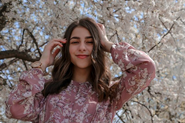 Smiling woman in a floral blouse under a blossoming tree