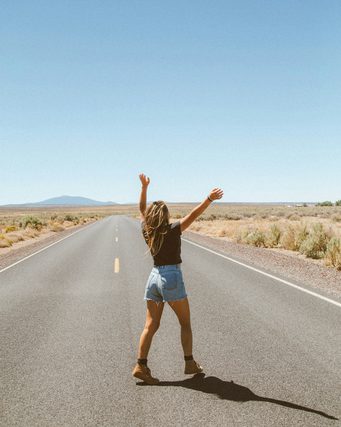 Woman with raised arms on an empty desert highway