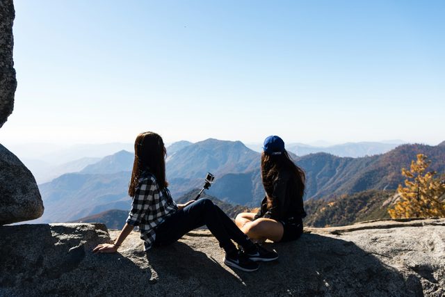 Two women sitting on a rock above a mountain valley