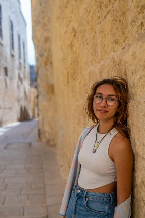 Woman in glasses and a white top leaning on a stone alley wall