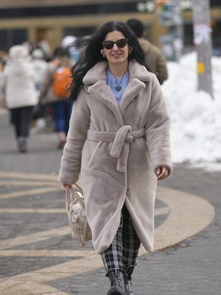 Smiling woman in a faux fur coat and sunglasses walking a snowy plaza