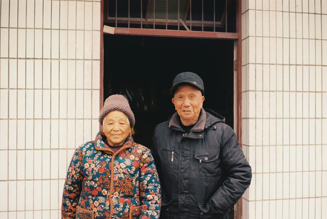 Elderly couple in winter coats standing in a tiled doorway
