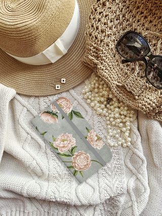 Straw hat, sunglasses, pearls and a floral case on a knit sweater