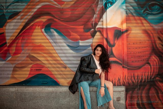 Woman in a leather jacket sitting by an orange and blue mural