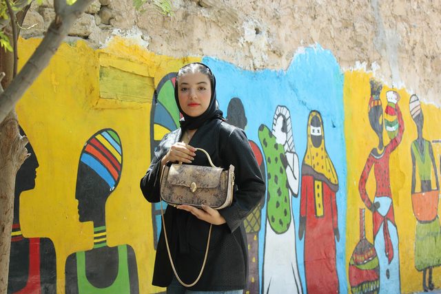 Woman in a black coat and headscarf by a painted yellow wall