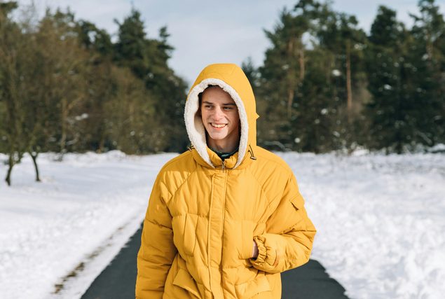 Young man in a yellow hooded parka on a snowy path