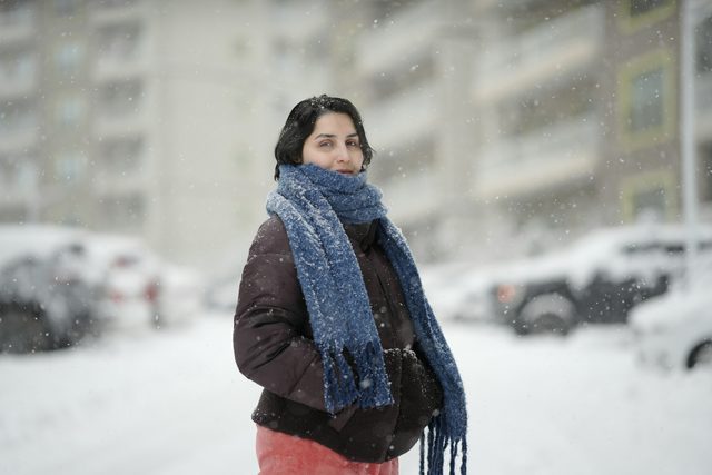 Woman in a brown jacket and blue scarf in falling snow
