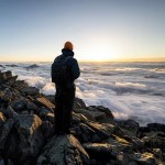 A hiker standing on rocks above the clouds at sunset