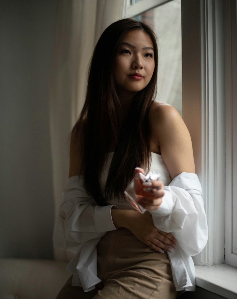 A woman in a white shirt sitting on a window sill in a neutral beige room