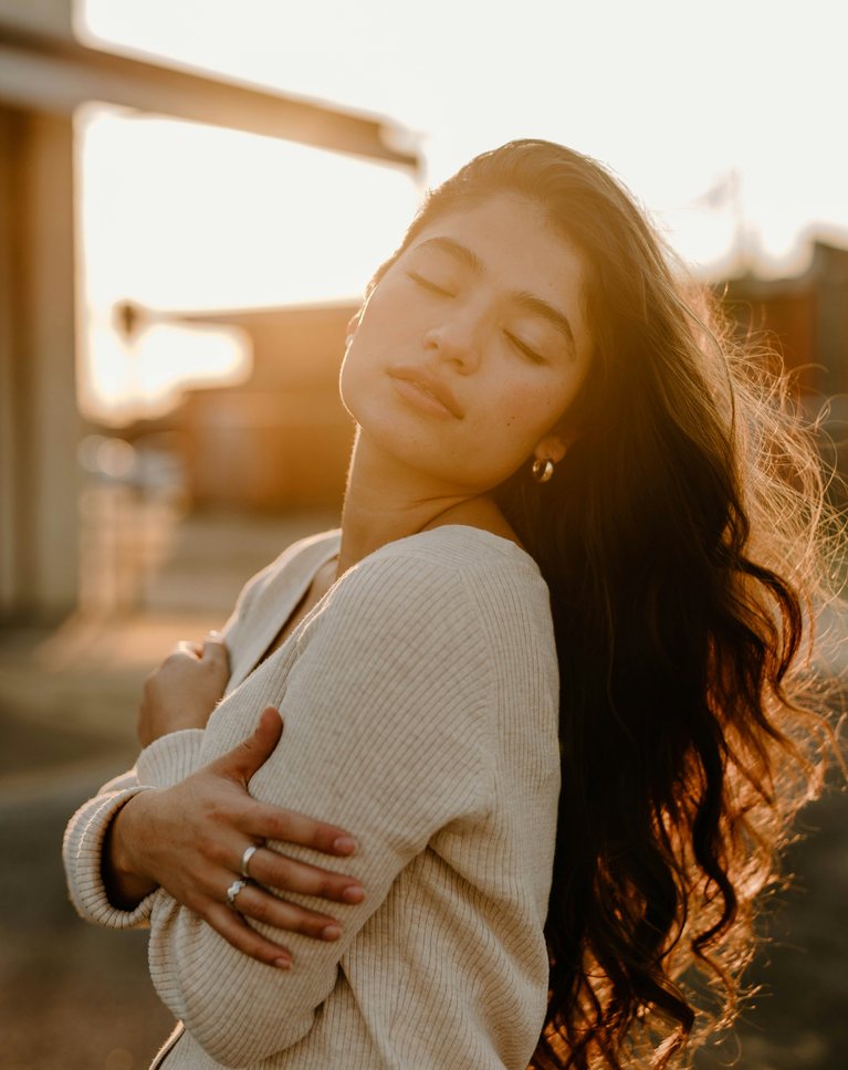 A woman in a cream knit sweater backlit at golden hour, with bright, warm highlights