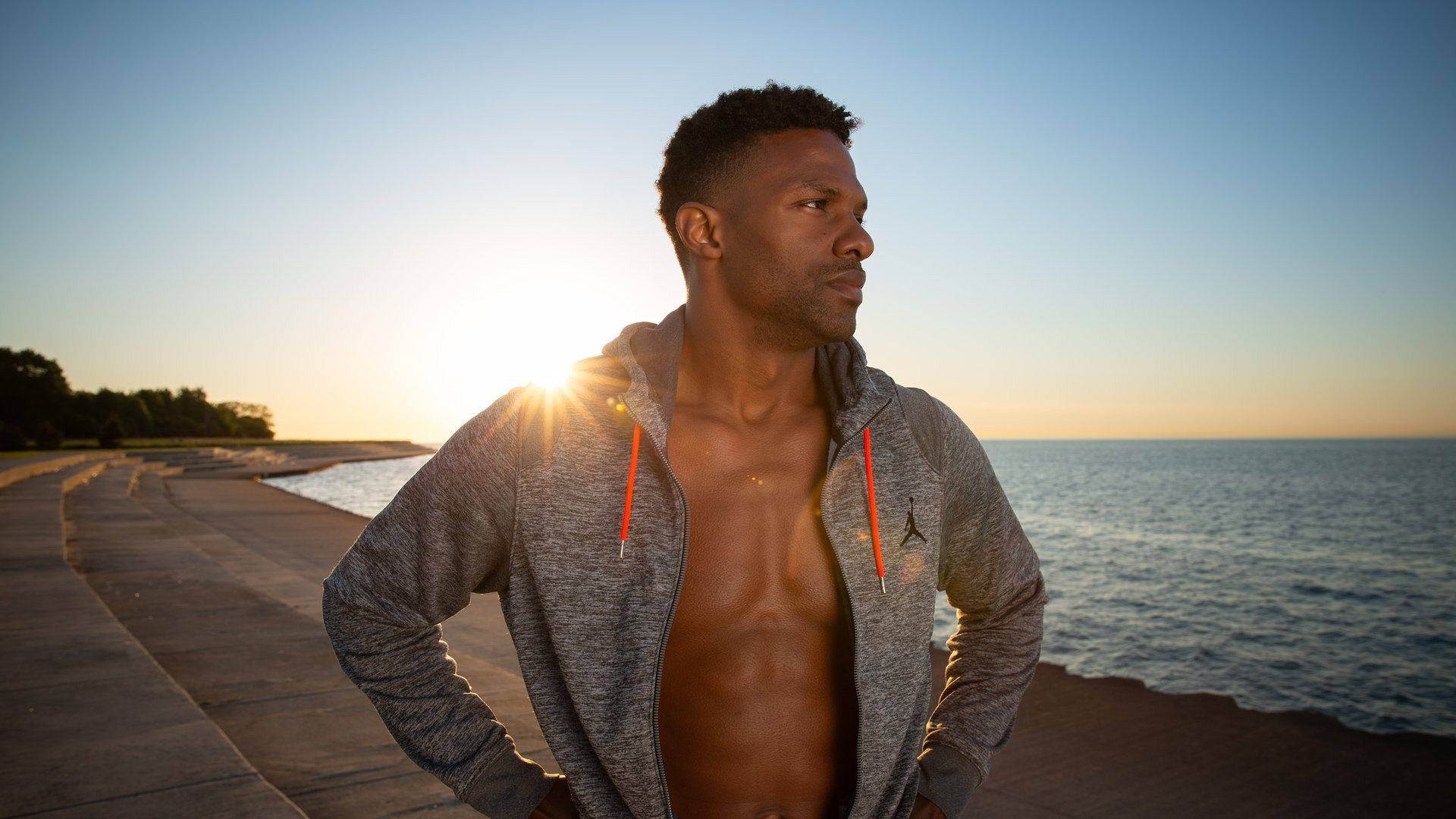A man in a gray hoodie on a lakefront at sunrise, with natural dark skin tones after skin tone correction in Camera Raw