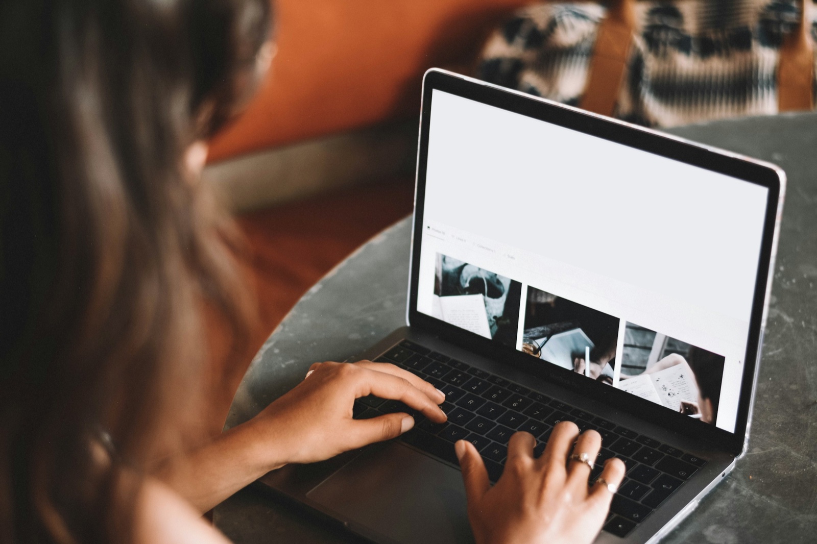 A woman at a table working through a page of photo thumbnails on a laptop