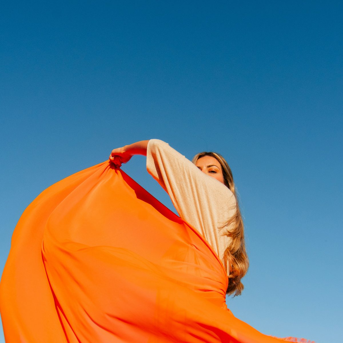 Complementary colors in photography: a woman holding up a length of flowing orange fabric against a clear blue sky