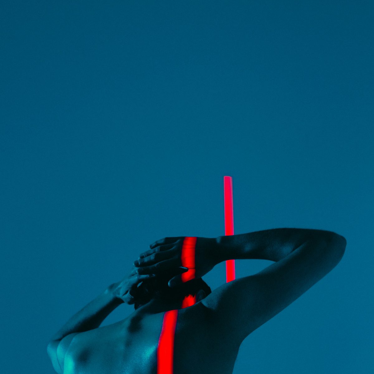 A person seen from behind in cyan light with a single stripe of red light down the spine