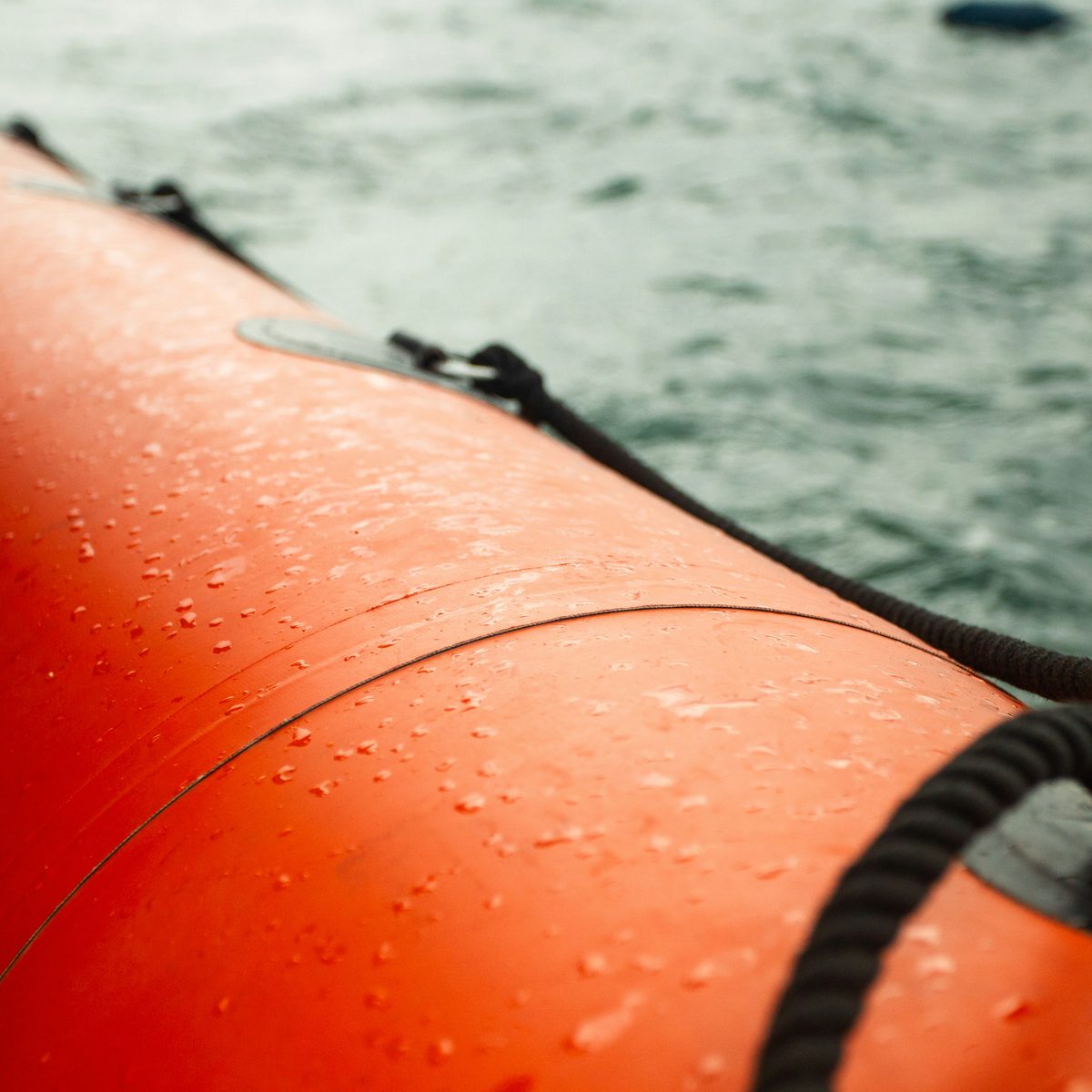 The orange side of an inflatable boat with water droplets against choppy grey-green water