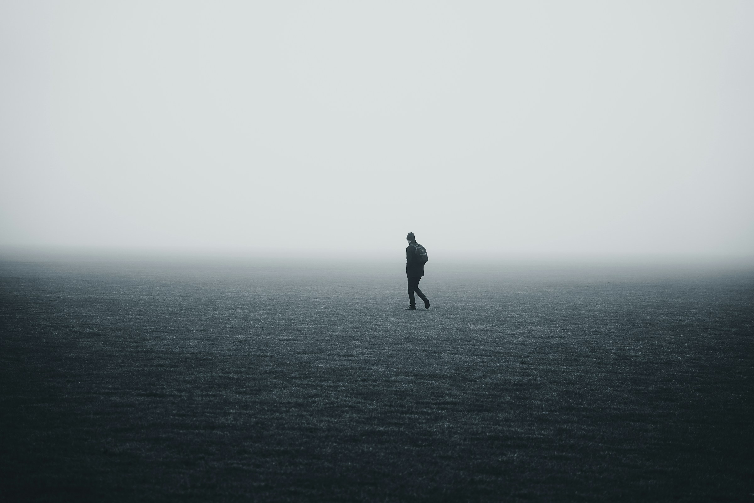 Lone figure walking across a dark field under a wide band of fog