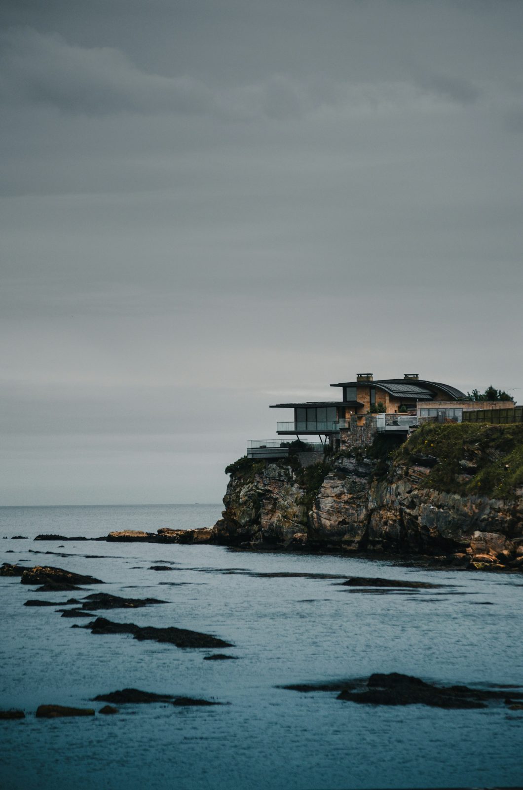 A clifftop house on a rock at the edge of the frame, balanced by a large grey sky and sea