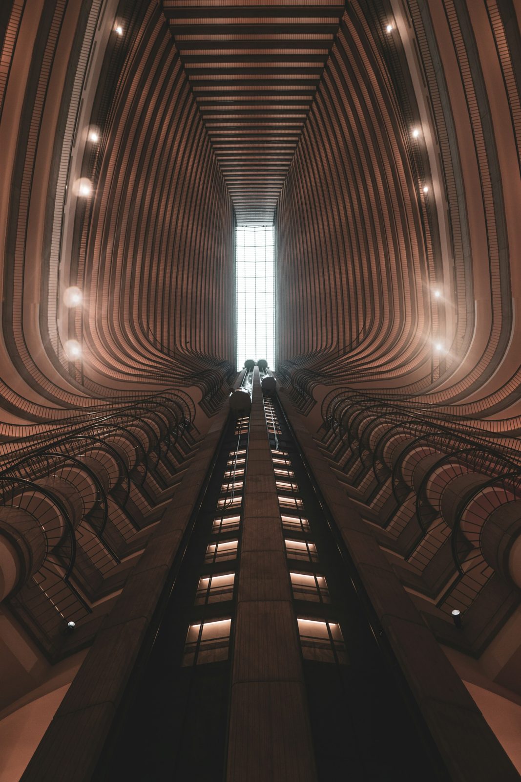 A symmetrical hotel atrium seen from below, with the glass elevators running up the centre line